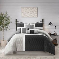 a bed with black and white comforters in a room next to a plant on a table