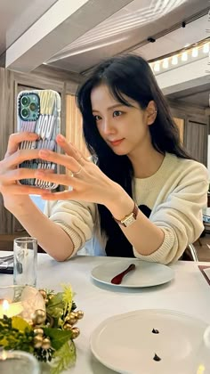 a woman sitting at a table taking a selfie with her cell phone in front of her