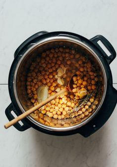 a pot filled with cooked chickpeas next to a wooden spoon on top of a white counter