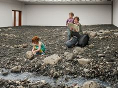 two children are sitting on rocks and looking at a book while another child sits in the water