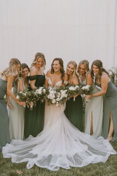 a group of women standing next to each other in front of a white wall holding bouquets