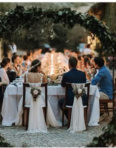 a group of people sitting at a table with white cloths and flowers in front of them