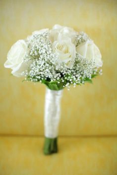 a bouquet of white roses and baby's breath sits on a yellow background,