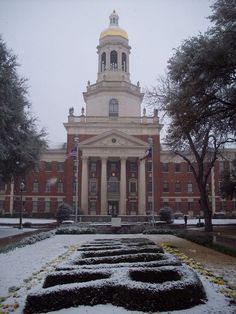 an old building with a clock tower in the background and snow on the ground around it