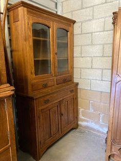 an old wooden china cabinet next to a tall piece of furniture in a room with white brick walls