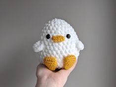 a hand holding a small crocheted white and yellow stuffed animal with black eyes