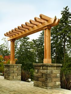 a wooden pergolated structure sitting on top of a brick walkway next to trees