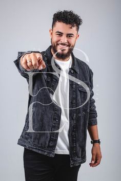 a man pointing at the camera while wearing a jean jacket and white shirt with black pants