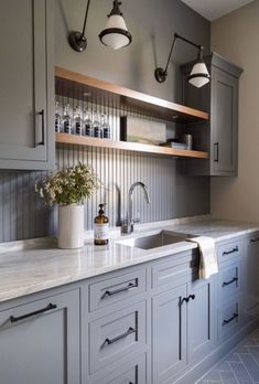 a kitchen with gray cabinets and marble counter tops, white tile flooring and hanging lights above the sink