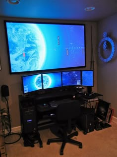 three computer monitors sitting on top of a desk in front of two large screen televisions