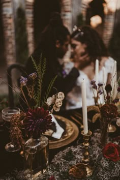 two people sitting at a table with flowers and candles