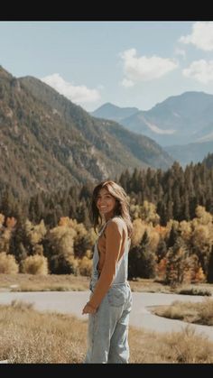 a woman standing on top of a grass covered field next to a forest filled with trees