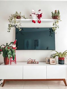 a flat screen tv sitting on top of a white shelf next to potted plants