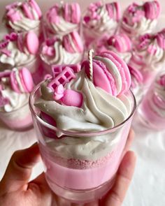 a hand holding a glass filled with pink and white desserts