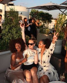 three women are sitting on a rooftop drinking wine and having fun with the cameraman