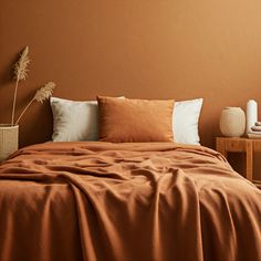 a bed covered in blankets and pillows next to a table with two vases on it