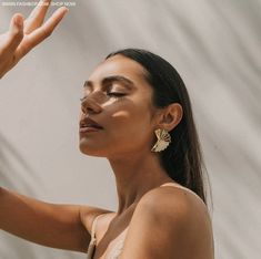 a woman with her hand up in the air while she is wearing gold earrings and a white tank top