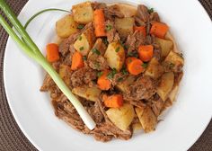 a white plate topped with meat, potatoes and carrots next to a green onion