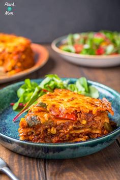 a blue plate topped with lasagna covered in cheese and sauce next to a salad