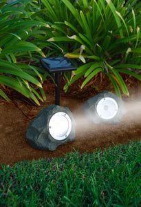 two lights are on in the ground near some grass and plants with green leaves behind them