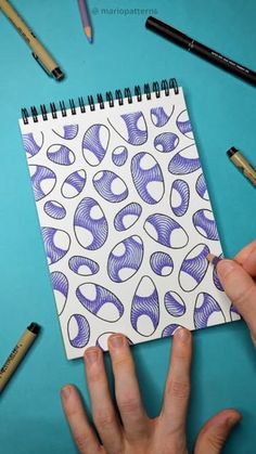 someone holding a notebook with purple and white designs on it, surrounded by crayons