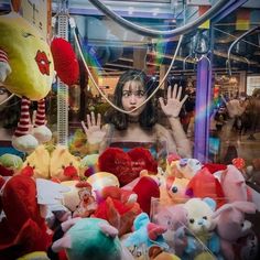 a woman is surrounded by stuffed animals in a store window with her hands up to the camera