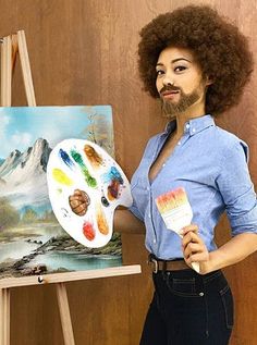 a woman standing in front of an easel holding two paint brushes and a palette