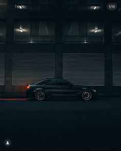 a black car parked in front of a tall building at night with lights on it