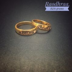 two gold wedding rings with names engraved on the sides, sitting on a black surface