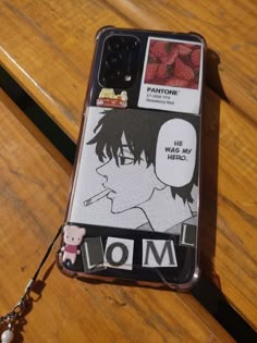 a cell phone case with an anime character on it sitting on a wooden table next to a keychain