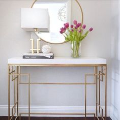 a white console table with flowers on top and a mirror above it in the corner