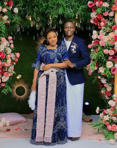 a man and woman standing in front of a floral arch