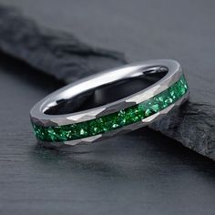 a wedding band with green stones in it on top of a piece of black wood