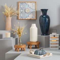 various vases and other decorative items on display in a room with gray walls, white flooring and wooden stools