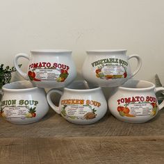 four white bowls with tomato soup on them sitting on a wooden table next to a potted plant