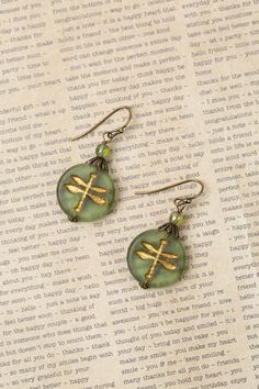 two green and gold earrings sitting on top of a piece of paper next to each other