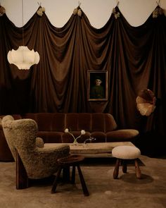 a living room with brown drapes and two chairs, a coffee table and ottoman