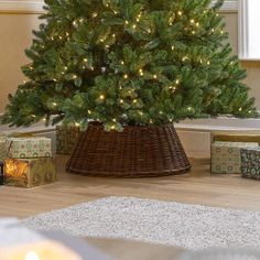 a christmas tree in a wicker basket with lights on the top and presents under it