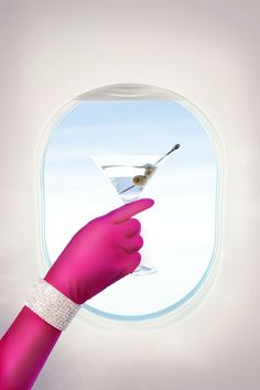 a hand holding a martini glass in front of an airplane window with a bird on it