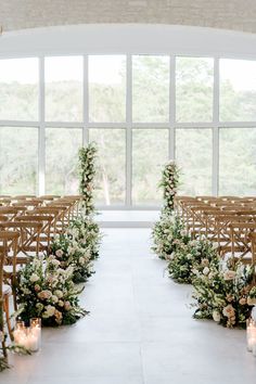 an indoor ceremony with rows of chairs and floral arrangements on the aisle, lit by candles