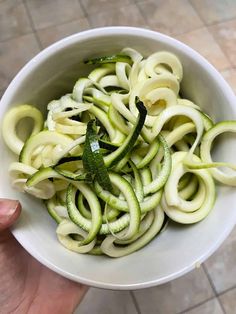 a person holding a white bowl filled with sliced zucchini and green pepper slices