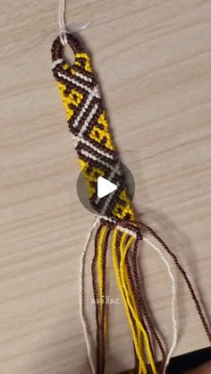 a hand holding a string with yellow and brown beads on it next to a wooden surface