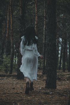 a woman in a white dress is walking through the woods