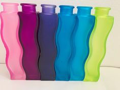 six different colored plastic bottles lined up in a row on a white surface, one is empty and the other has no lid