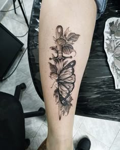 a black and white photo of a butterfly tattoo on the right leg, with leaves around it