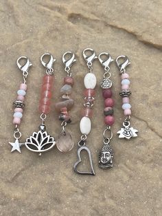 several different bracelets with charms attached to them on a beach sand surface in front of a rock