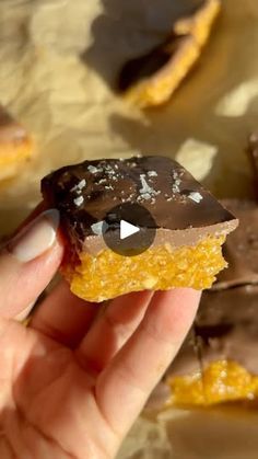 a person holding up a piece of chocolate and orange slice with white sprinkles