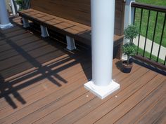 a wooden deck with white pillars and potted plant on it's side area