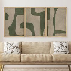 two abstract paintings hang on the wall above a couch in a room with white walls