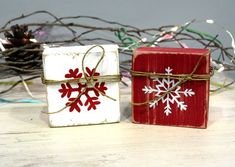 two small boxes with snowflakes tied to them on a table next to a pine cone